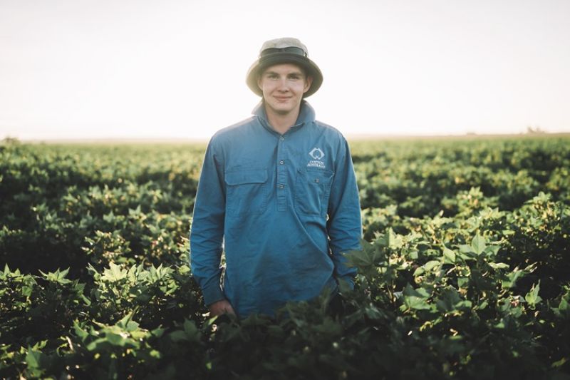 Farmer wearing blue shirt and a sun hat standing in a field. Green crop in background