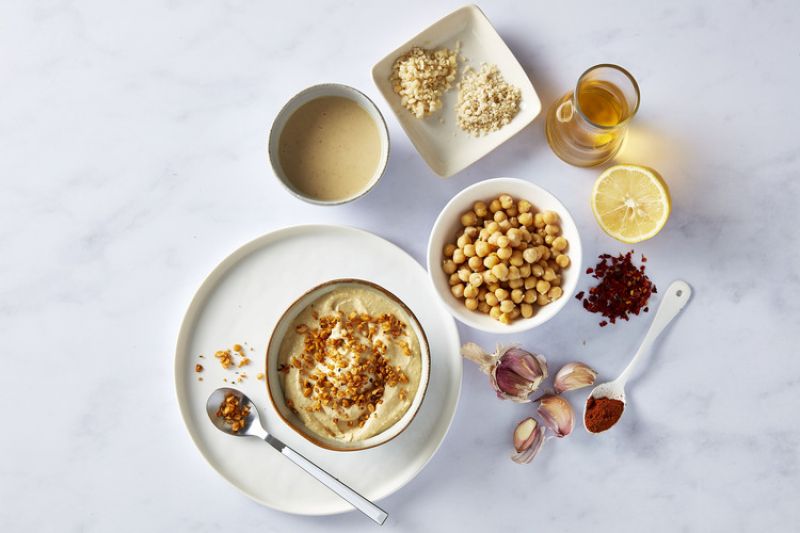 Hummus in a bowl, surrounded by condiments