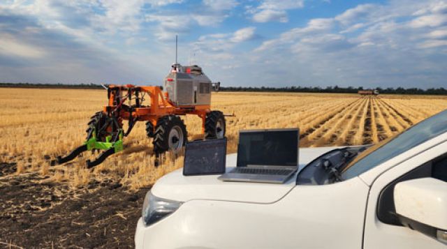 Two laptops on a ute monitor an orange SwarmFarm robot surveying a stubble paddock for electromagnetic soil mapping.