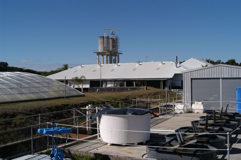 Industrial research facility with water tanks, pipework, sheds and a tall water tower under a clear blue sky.
