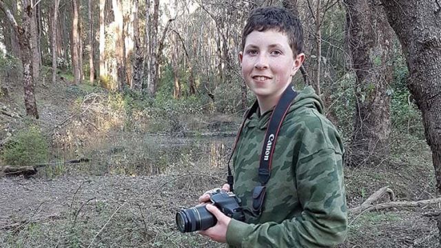 Student holding a camera in bushland near a creek.