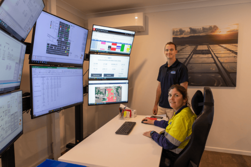 A man and a woman wearing Tassal work shirts are looking at several computer monitors that display data about various operations around Tassal’s facility. 