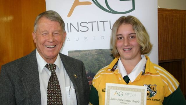 A student holds a certificate beside an older man at an awards display.