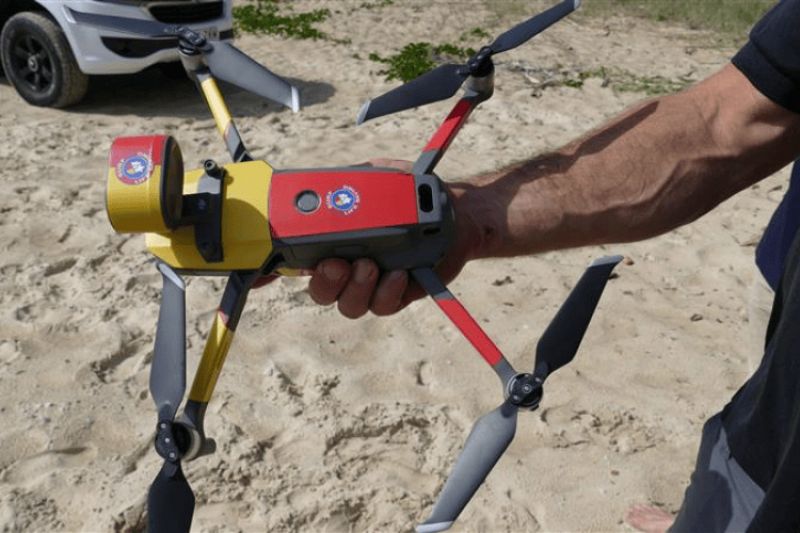 A red and yellow drone is being held in hands at the beach.
