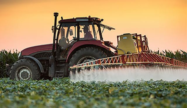 A tractor spraying crops at sunset in a large field, highlighting sustainable farming practices