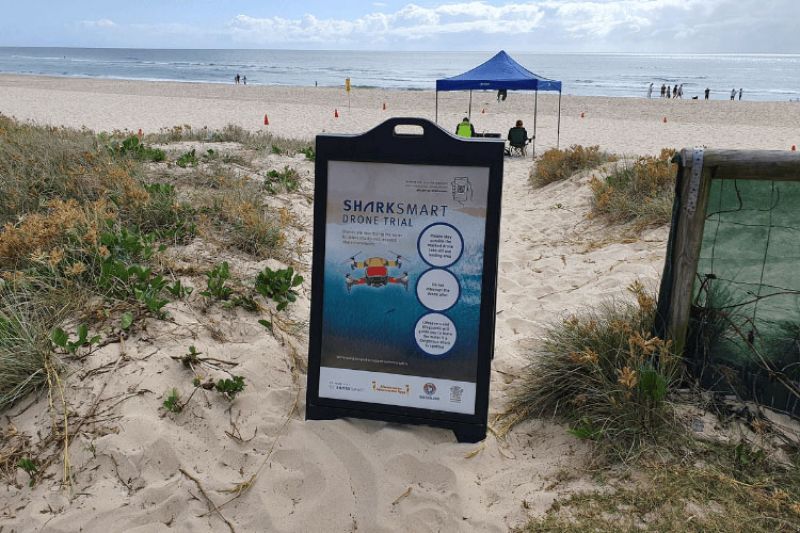 A Gold Coast beach with a sign highlighting the SharkSmart drone trial is in action.