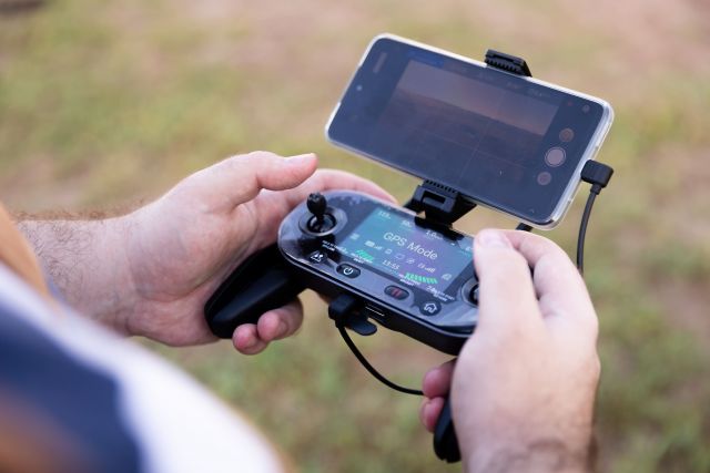 Close-up of hands holding a drone controller with smartphone screen in GPS mode.