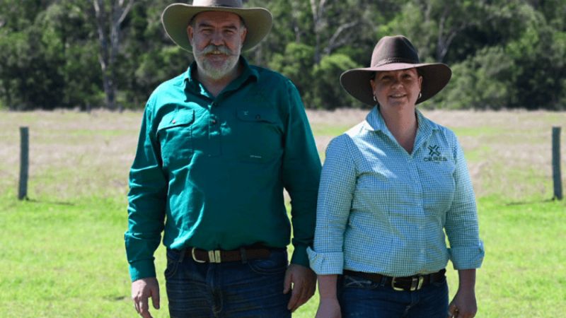 A man and woman stand in a grassy field wearing wide-brimmed hats and green collared shirts with 'Ceres Tag' on them.